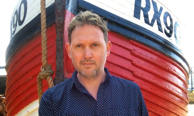 Portrait of Thomas Taylor standing in front of an old wooden fishing boat with a red, black and white hull
