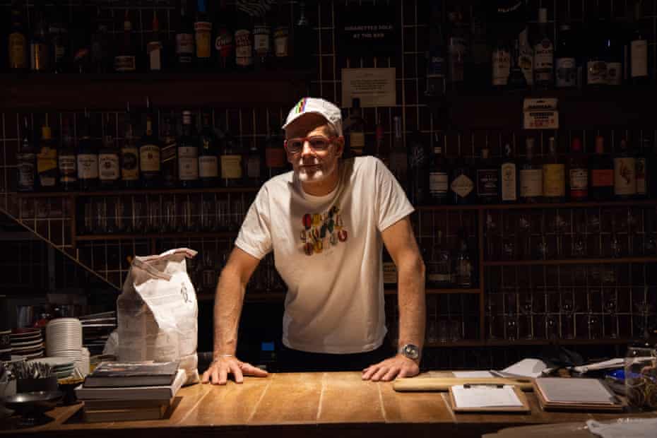 The man is standing in a dark bar with his hands on a bench