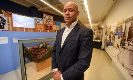 Marvin Rees stands in front of the toppled statue of Edward Colston, which is lying horizontal in a glass case.