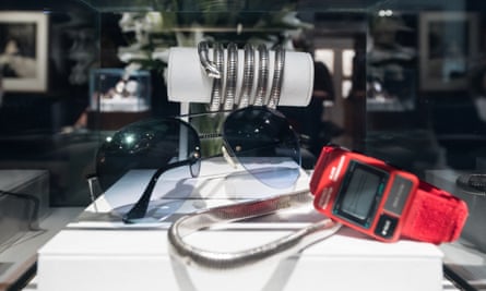 A silver snake bangle next to a pair of sunglasses and a watch.