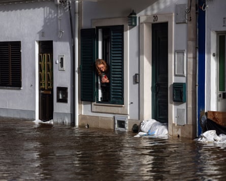 A woman leans out of her window to take a picture of the flooded street