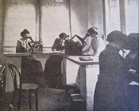 Victorian-era women peering through what look to be microscopes in a room