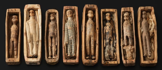 A row of wooden coffins, only 9.5cm long, containing wooden figures each dressed differently