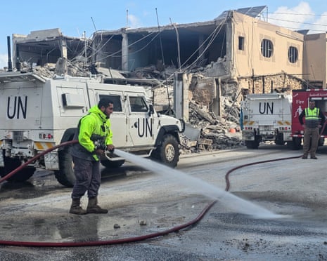 यूनिफिल शांतिरक्षक शुक्रवार को दक्षिणी लेबनान के नक़ुरा क्षेत्र में इजरायली हवाई हमले के स्थल पर सड़क साफ कर रहे अग्निशामकों के पास से गुजरे।