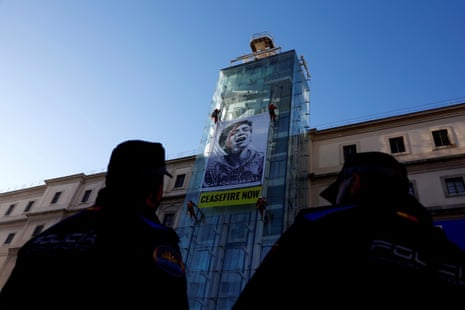 Police officers keep watch as Greenpeace activists unveil the illustration ‘Obey’ by US artist Shepard Fairey, which depicts a photograph by Gazan photojournalist Belal Khaled of a Palestinian child crying for help, next to a banner reading: ‘Ceasefire now’, outside Reina Sofía museum in Madrid, Spain on Wednesday.