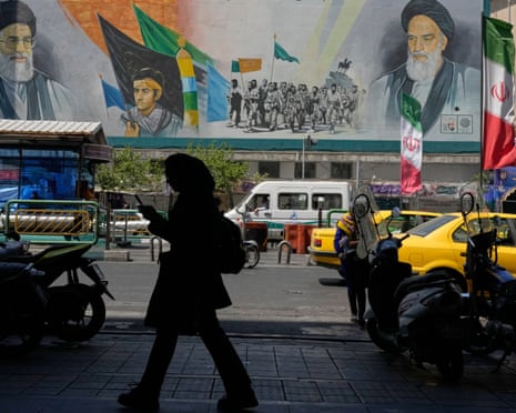 A woman in silhouette walks past a large mural showing two portraits and soldiers with flags