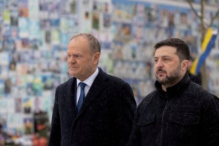 Donald Tusk and Volodymyr Zelenskyy walk beside a wall covered in photos of Ukrainians killed in the country’s war with Russia