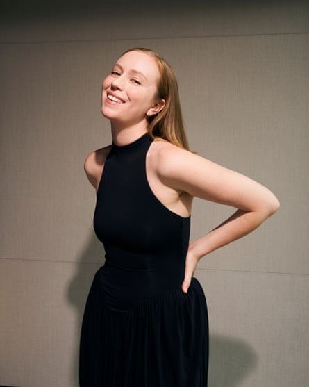 A woman in a black dress smiles and poses casually.