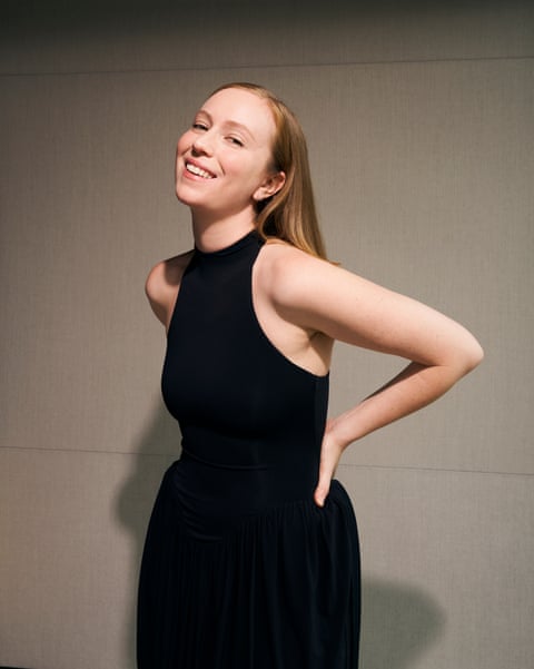 A woman in a black dress smiles and poses casually.