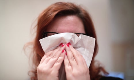 A woman with a cold blows her nose with a tissue.