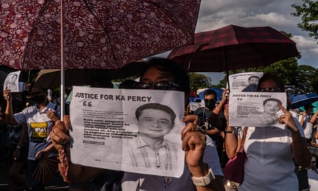 A crowd of people hold up umbrellas and pieces of paper titled 'Justice for KA Percy' with a photograph of Percival Mabasa