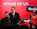 People take pictures on their phones of Starmer giving a speech