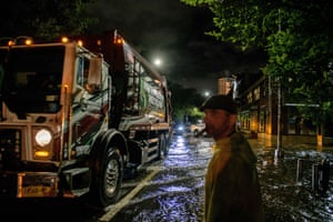 A refuse collection worker checks the depth of a flooded street before driving his truck through in Brooklyn