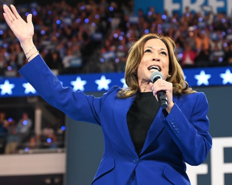 Kamala Harris in a blue suit, speaking into a mic gestures with one hand raised