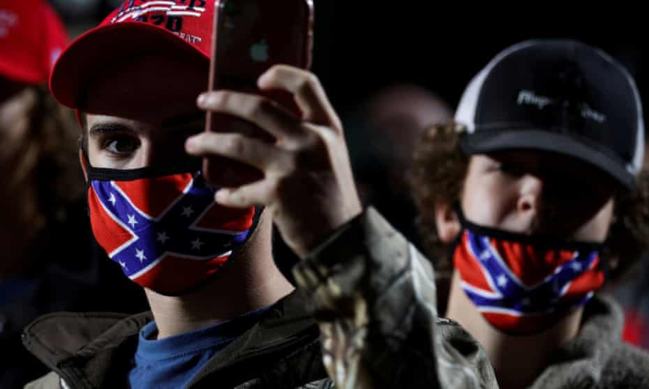 A man wearing a face mask featuring the Confederate battle flag holds a mobile phone during a Trump rally in Georgia.