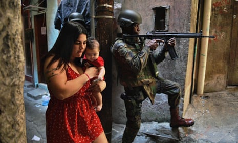 In this file photo taken on 23 September 2017 a woman walks with her baby past a militarized police soldier in the Rocinha favela in Rio de Janeiro, Brazil.