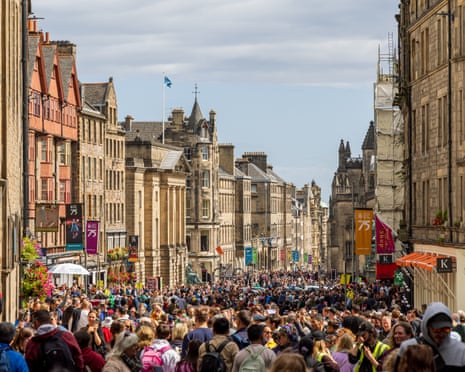A dense crowd fills Edinburgh's Royal Mile, lined with stone buildings and colorful banners