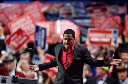 man in a red shirt and suit in front of a big crowd waving signs