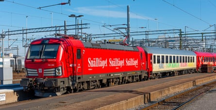 A red engine with carriages at a platform against a blue sky