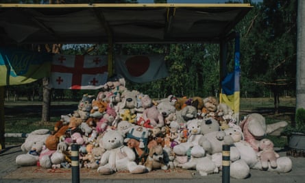 A pile of cuddly toys at a bus stop with flags behind, one Ukrainian