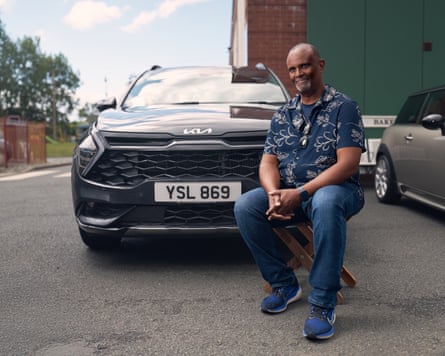 A man sitting in front of a black Kia with the number plate “YSL 869”