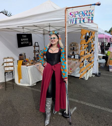 A woman dressed in a colorful headdress, long skirt and boots posing beside a festival pop-up tent that is labeled Spork Witch.