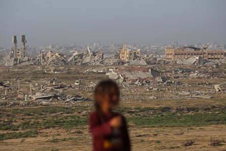 A Palestinian girl stands against the backdrop of destroyed buildings