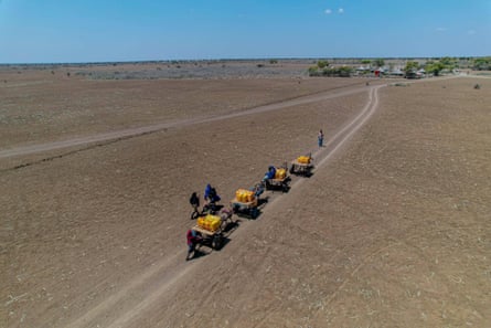 Aerial shot of people on carts with big yellow water containers approaching a newly built borehole in a parched landscape