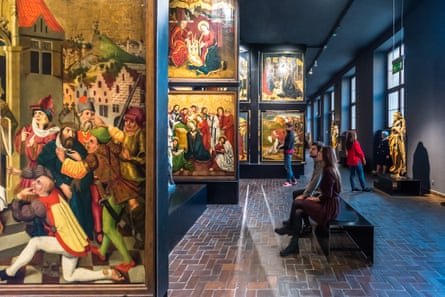 Visitors sitting and standing in front of religious paintings in a gallery.