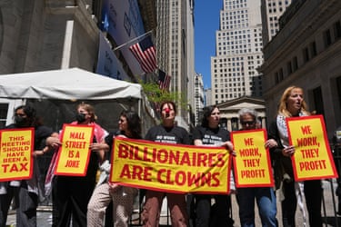 people hold signs that read ‘billionaires are clowns’ and ‘we work they profit’