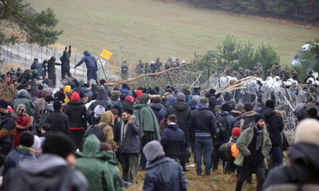 Migrants gather on the Belarusian side of the border as Polish officers look on.