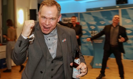 A male AfD supporter celebrates after the Bavarian state elections in Munich dressed in grey 3-piece suit and carrying a beer bottle