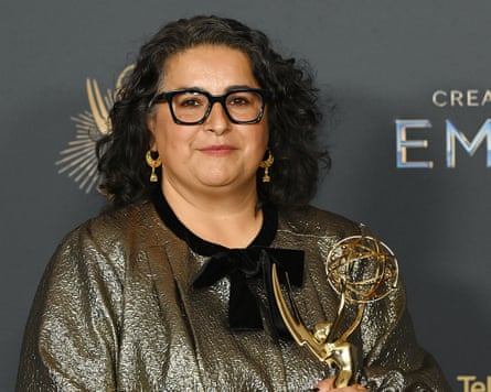 Shaheen Baig holds her Emmy award, wearing a muted gold dress