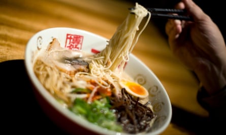 A bowl of ramen made wtih noodles and a hard boiled egg being eaten with chopsticks