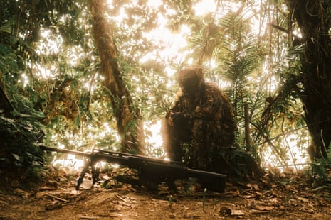An ELN member wearing camouflage used by the group’s snipers sits against a tree with a precision rifle