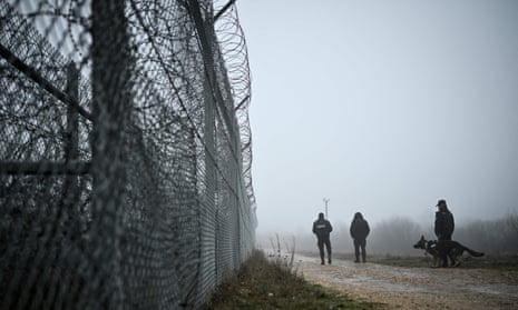 Bulgarian border police officers patrol with a dog in front of the border fence on the Bulgaria-Turkey border near the village of Lesovo