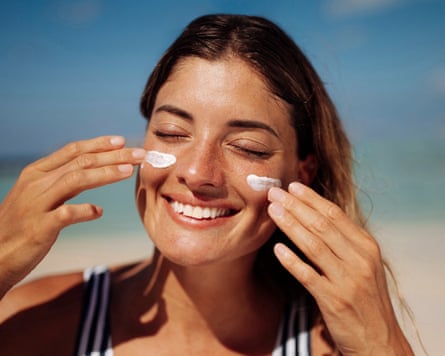 A woman applying sunscreen to her face at the beach