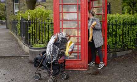 A woman collects food from a disused traditional red phonebox converted into a free community foodbank