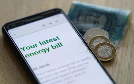 An energy bill on a mobile phone on a table, with coins and a £5 note