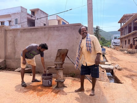 A man pumps water on a street corner against a backdrop of a concrete wall.
