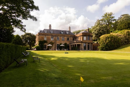 A historic stone building is seen across a green croquet lawn.