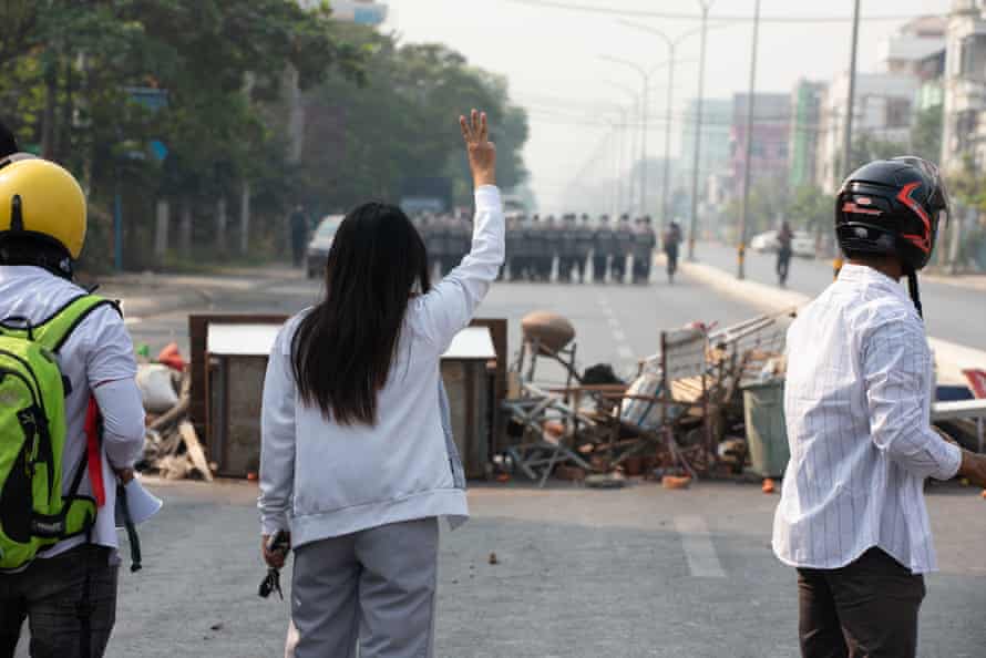 A woman makes a three-fingered salute at soldiers from behind a makeshift barricade, on a street in Mandalay.