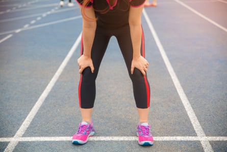 Woman suffering from painful knee while running on the blue rubberised running track