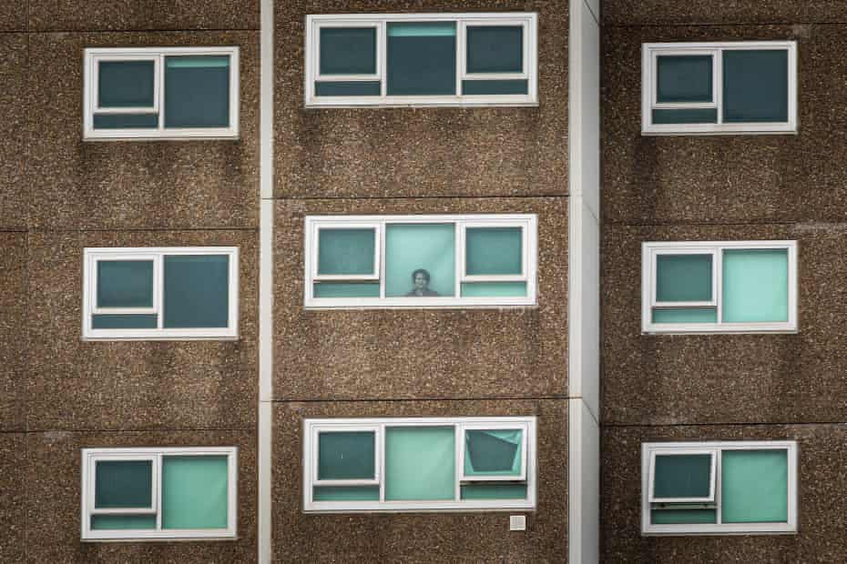 A lone woman is seen looking out the window of her apartment in North Melbourne