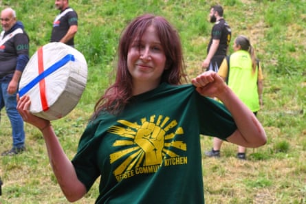 Ava points to her Refugee Community Kitchen T-shirt while holding a wheel of cheese
