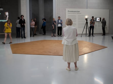 A crowd of people stand around the finished hexagon of peanut butter in the gallery