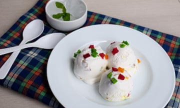 White plate of three scoops of vanilla ice cream with tutti-frutti jelly sprinkles on the top, sitting on a checked place mat with a couple of spoons next to it