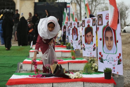 A woman spreading flower petals over a grave draped with an Iranian flag, and showing a picture of a young girl