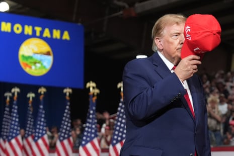 Donald Trump holds a red cap in front of his face