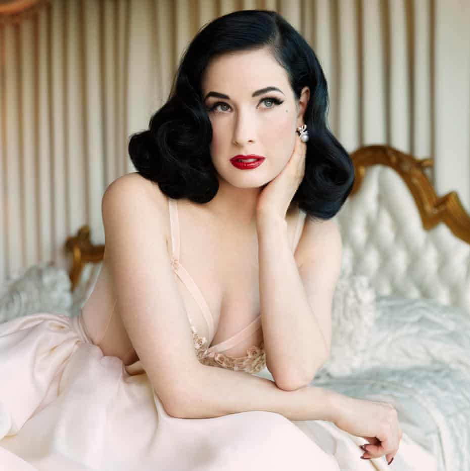Dita sitting on a bed wearing a white dress